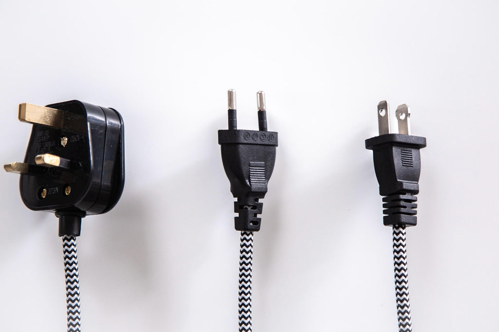 Three black electrical wall plugs of different types connected to braided black-and-white cords, arranged vertically against a plain white background.