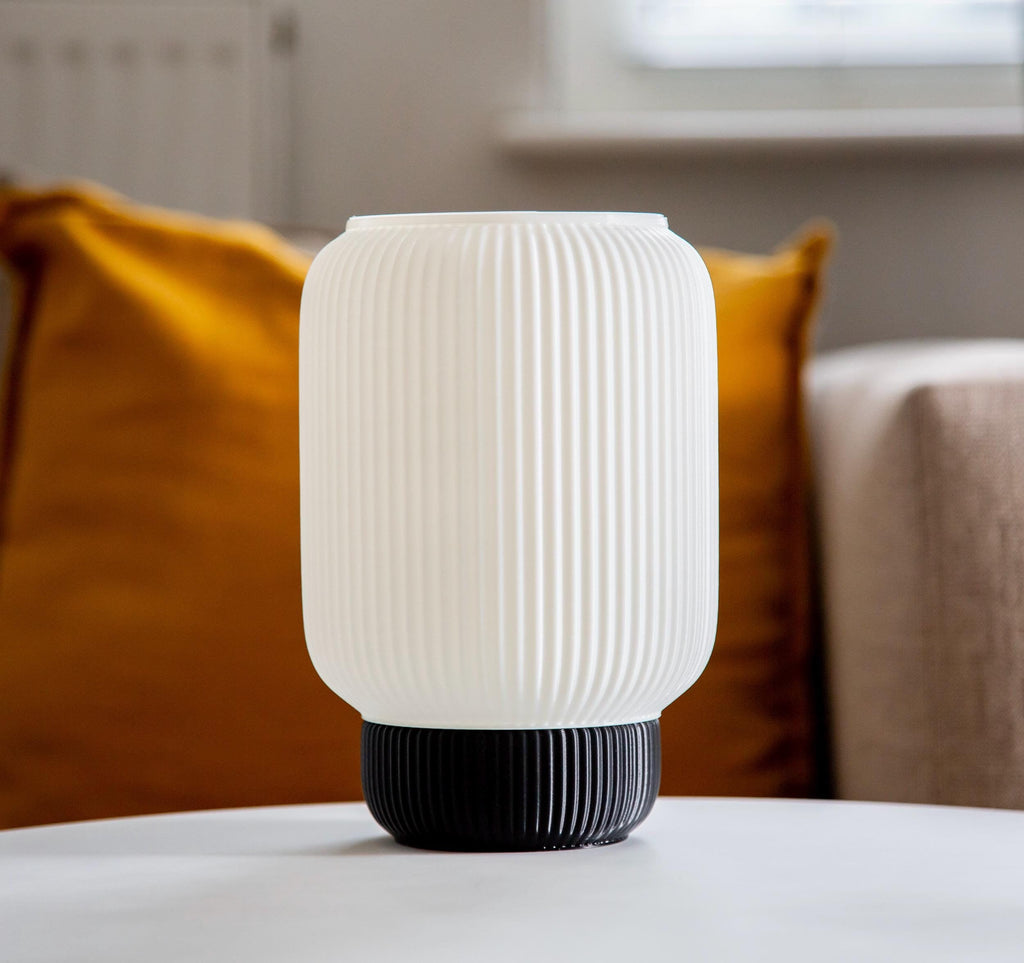A ribbed translucent white Plasticlampshade with a black fluted base, displayed on a white surface against a neutral gray background.