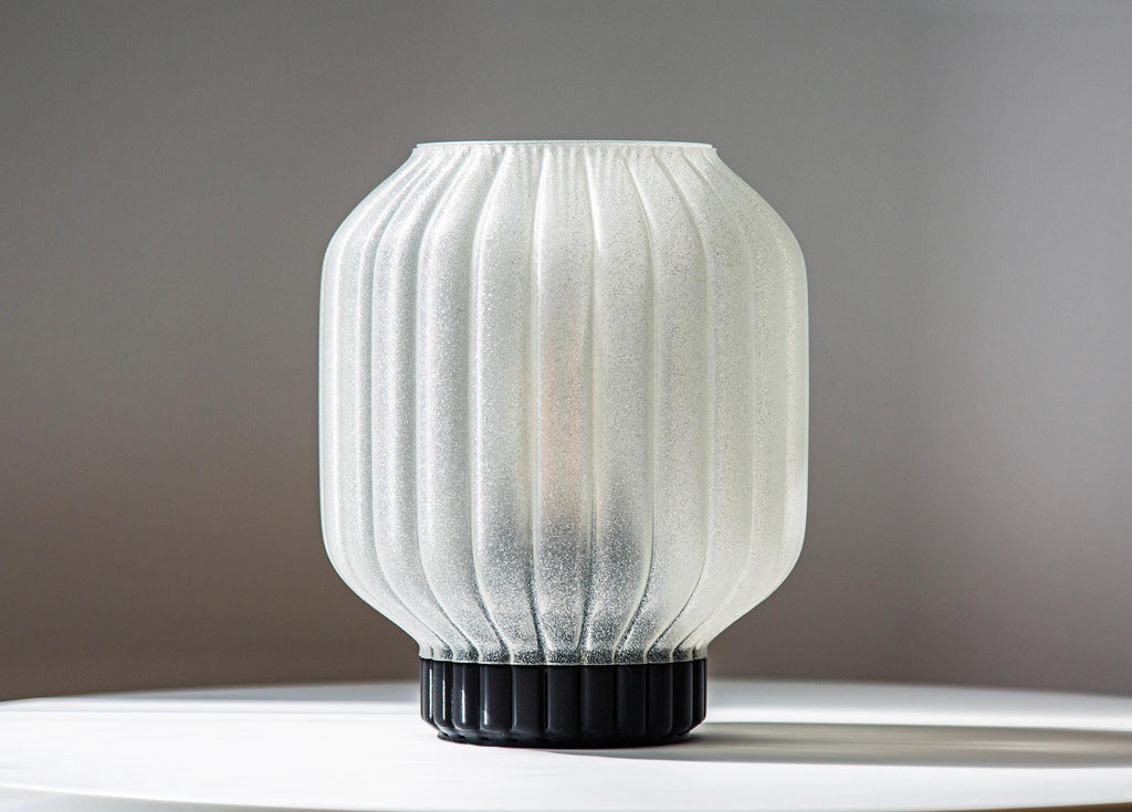 A ribbed translucent white glass lampshade with a black fluted base, displayed on a white surface against a neutral gray background.