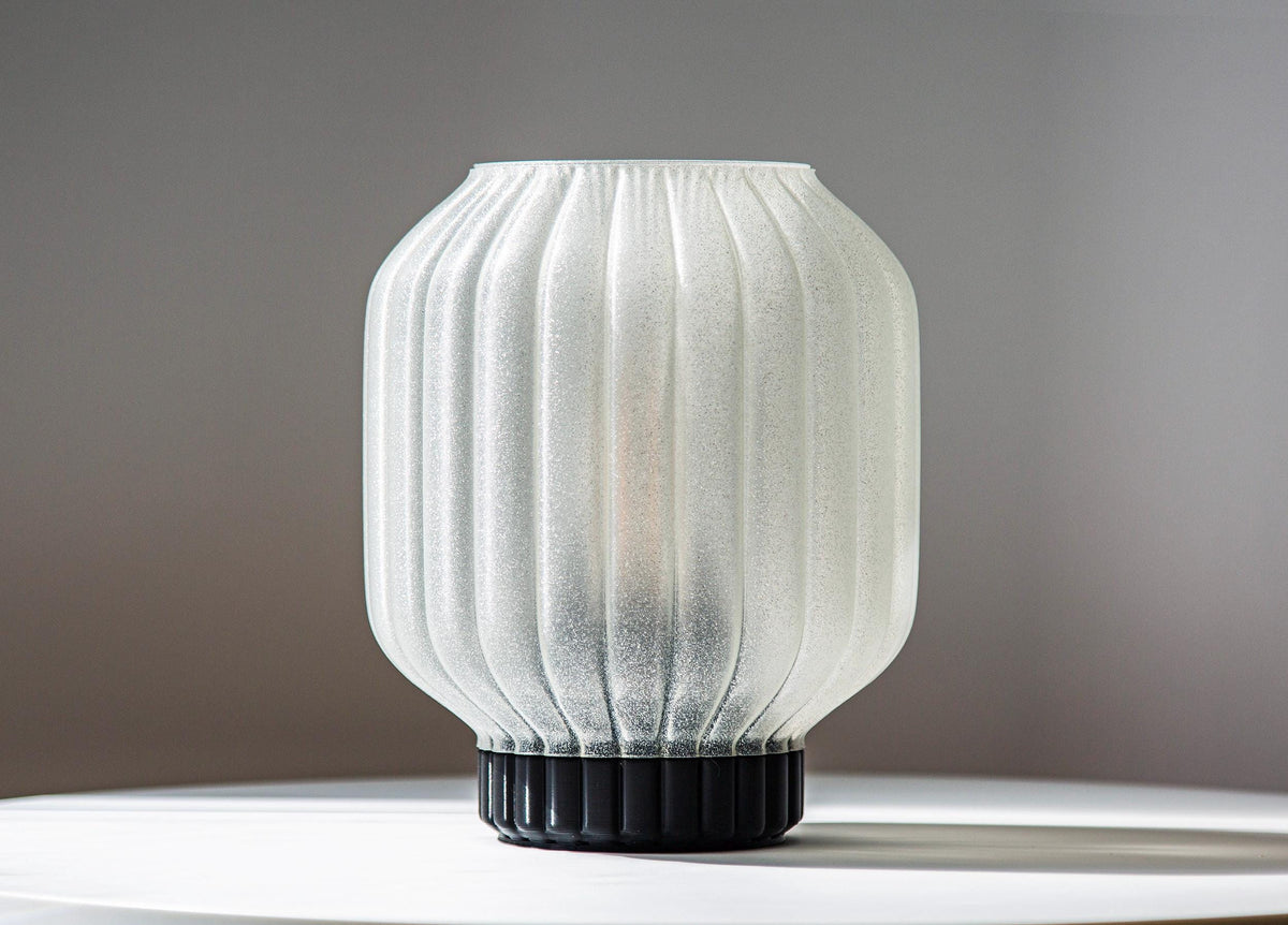 A ribbed translucent white glass lampshade with a black fluted base, displayed on a white surface against a neutral gray background.