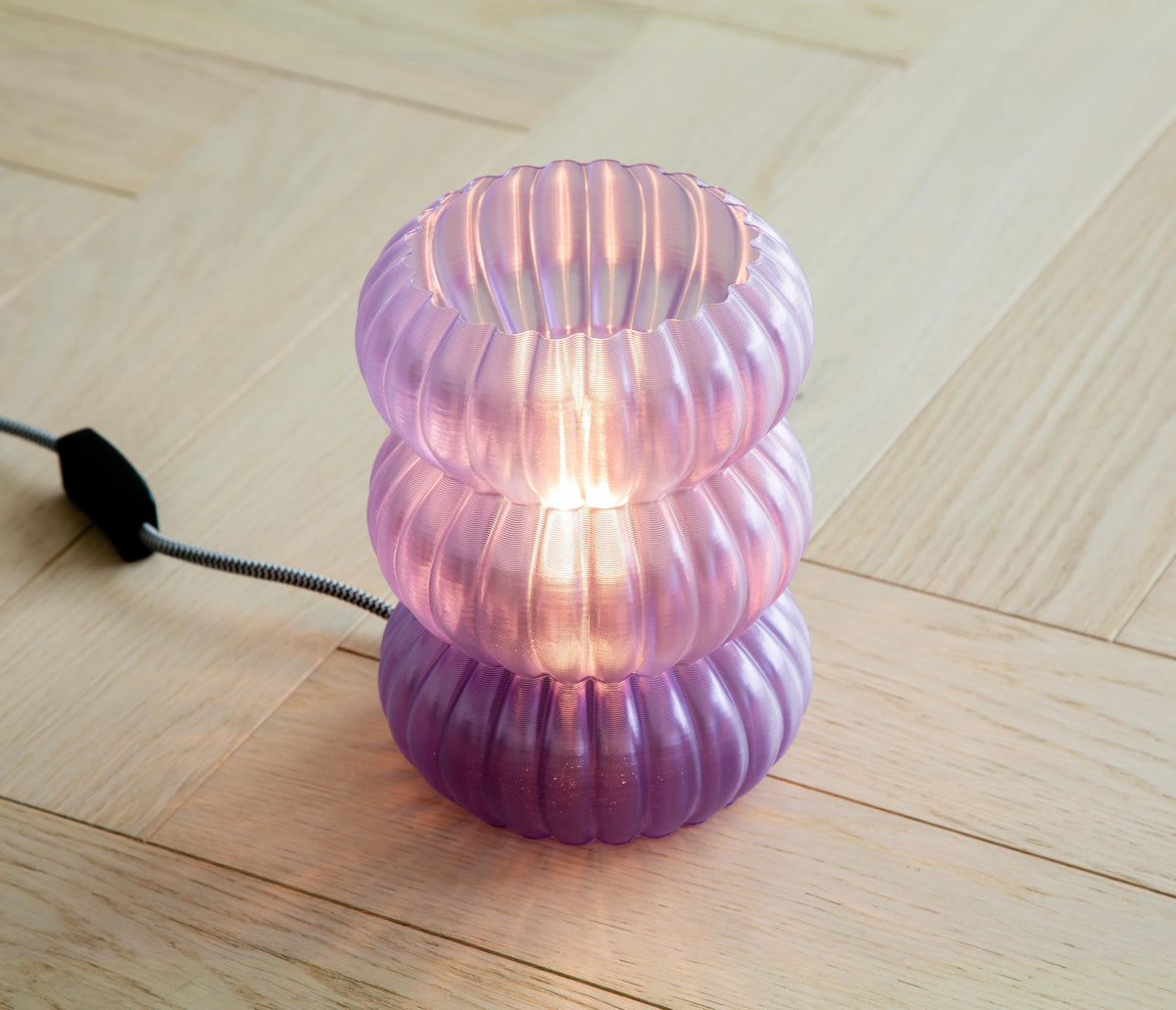 A modern pendant light with a flared, layered shade made of translucent warm white material, glowing with a soft golden light against a dark gray background.