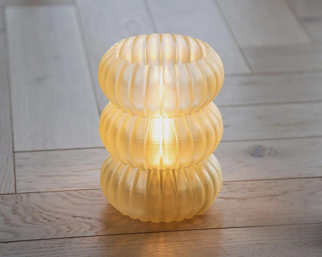 A ribbed translucent white lampshade with a black fluted base, displayed on a white surface against a neutral gray background.